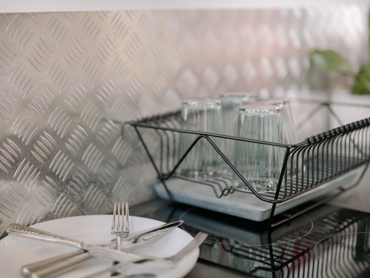 Close-up of a kitchen dish rack with glassware and utensils on a clean countertop.